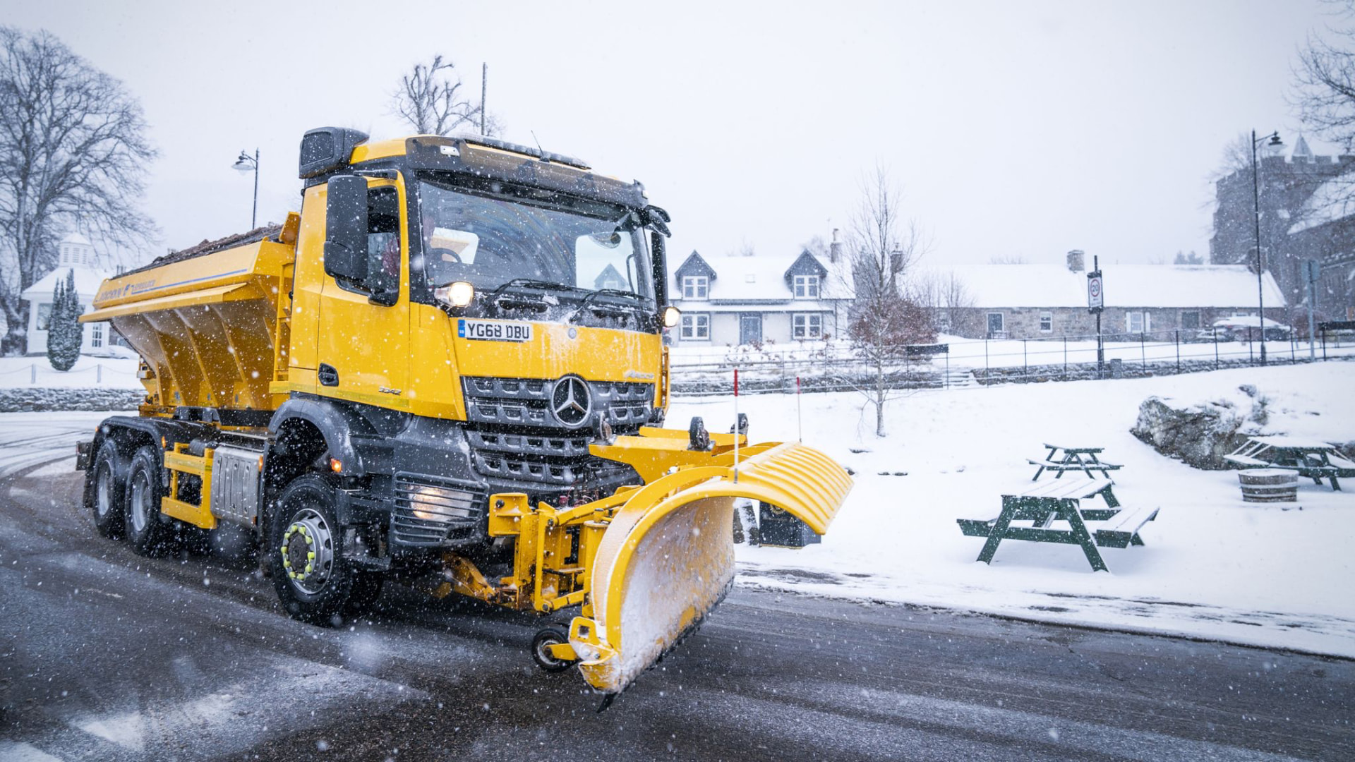 Yellow gritter truck clearing snow and treating a commercial site car park